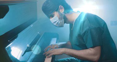 Üniformalı ve maskeli bir doktor piyano çalıyor. 