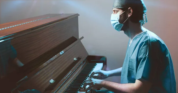Üniformalı ve maskeli bir doktor piyano çalıyor. 