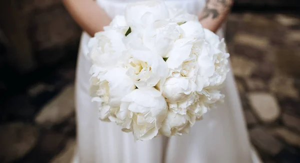 Hermoso ramo de boda blanco de peonías en las manos de la novia en un vestido blanco —  Fotos de Stock