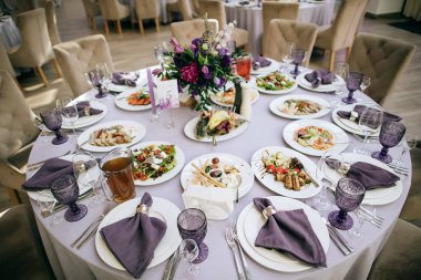 Zarif masa seti. Mor renkte güzel bir düğün restoranı dekorasyonu: mor bardaklar, mor çiçekler ve peçeteler