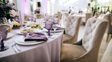 Masa hazır. Mor renkte güzel bir düğün restoranı dekorasyonu: mor bardaklar, mor çiçekler ve peçeteler