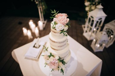 Düğün pastası. Düğün kemeri ve mumların arkasında beyaz ve pembe çiçekler var.