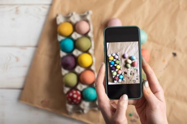 Cep telefonu tutan ve Paskalya süslerinin fotoğrafını çeken bir kadın.