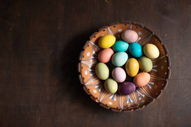 Ahşap masanın üzerinde renkli paskalya yumurtaları olan bir kase. Mesaj için yer var. Mutlu Paskalyalar.