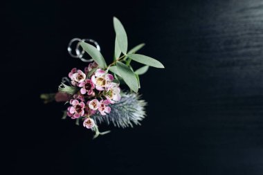 Damat yaka çiçeği ve alyanslar koyu arkaplanda.