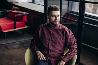 Bir kafede oturan sakallı genç adamın portresi.