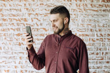 Dövmeli genç sakallı adam video görüşmesi için cep telefonu kullanıyor.