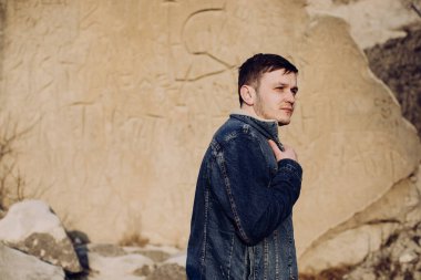 Genç adam kaya duvarına yaslanıyor.