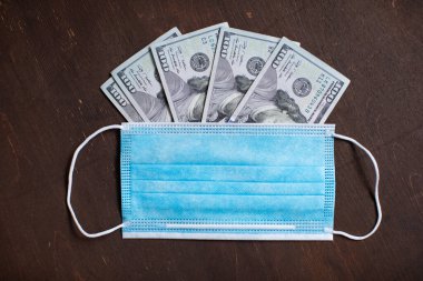 Para, dolar banknotları ve tahta arka planda koruyucu bir tıbbi maske. ABD 'deki koronavirüs salgını sırasında ekonomik ve sosyal sorunlar kavramı