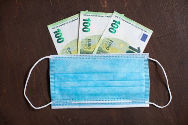 Para, Euro banknotları ve ahşap arka planda koruyucu bir tıbbi maske. Avrupa 'daki koronavirüs salgını sırasında ekonomik ve sosyal sorunlar kavramı