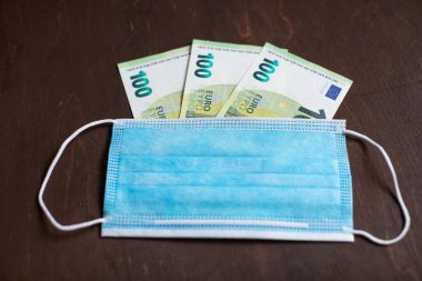 Para Euro ve tahtadan bir arka planda koruyucu tıbbi maske. Bir salgın ve salgın sırasında ekonomik sorunlar kavramı