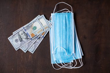 Koruyucu tıbbi maskeler ve para dolarları ahşap bir masada yatıyor.