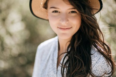 Hasır şapkalı güzel bir kadın kameraya bakıyor.