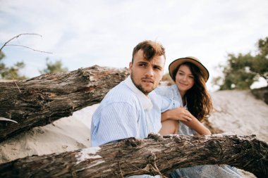 Genç bir çift sahilde yaşlı bir ağacın yanında oturuyor.