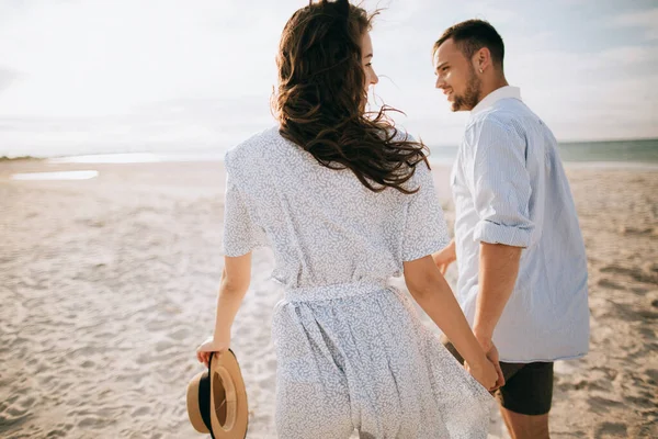 Young couple walking on the morning sea beach holding hands