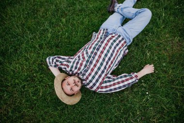 Hasır şapkalı genç çiftçi yeşil çimlerin üzerinde yatıyordu.