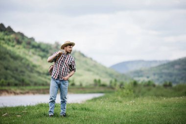 Sırt çantalı, hasır şapkalı genç hippi yeşil dağlara seyahat ediyor.