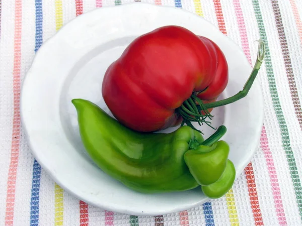 Huge tomato and atypically grown green pepper on white plate — Stock Photo, Image