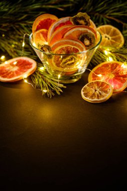 Yaratıcı karamsar Noel tatili. Yeni yıl meyveleri. Kurutulmuş greyfurt, kivi, portakal ve limon. Köknar ağacının dalında sıcak ışıklar, açı açısı, uzay kopyası.