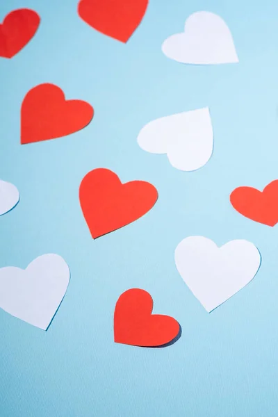 Red and white handmade paper hearts valentines on blue background, angle view, selective focus