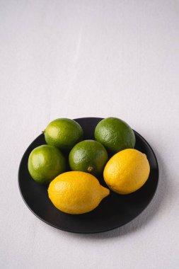Beyaz arka planda siyah tabakta limon ve ekşi meyveler, açı, vitaminler ve sağlıklı yiyecekler.