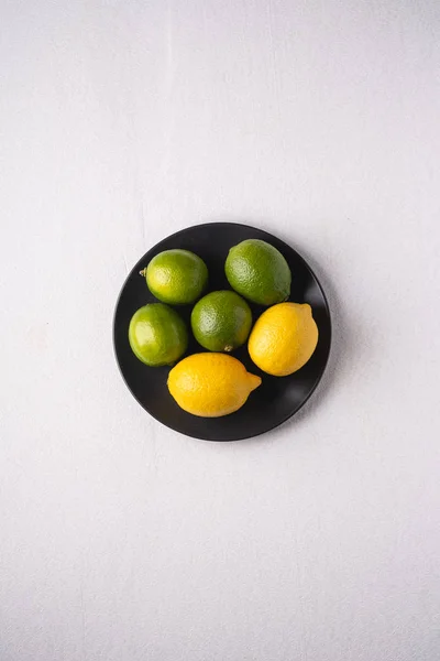 Beyaz arka planda siyah tabakta limon ve ekşi meyveler, üst manzara, vitaminler ve sağlıklı yiyecekler.