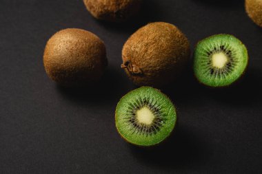 Kiwi fruits half sliced on dark black moody plain background, copy space, top view