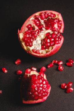 Taze, tatlı, kabuklu nar, koyu siyah arka planda kırmızı tohumlar, açı görüşü, seçici odak, sağlıklı besin meyveleri.