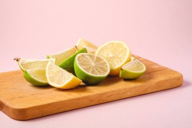 Taze limon ve limonlu narenciye dilimleri ahşap kesme tahtasında, minimum pembe arka plan izole edilmiş, açı görüşlü.