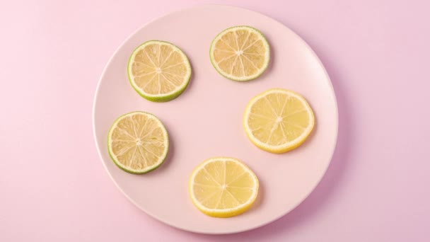 新鲜美味的柠檬和石灰片旋转在粉红盘上 停止运动动画4K视频与柑橘类水果的最小背景 顶部视图 — 图库视频影像