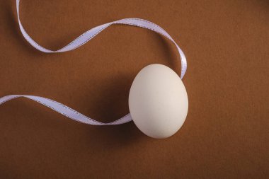Kahverengi kağıt arka planda kumaş kurdeleli tek beyaz yumurta, üst manzara, mutlu Paskalya günleri.