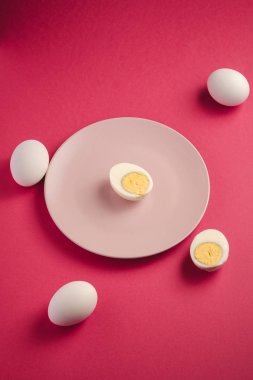 Haşlanmış yumurta sarısı pembe tabakta, beyaz yumurtaların yanında canlı kırmızı arka plan, açılı manzara, mutlu Paskalya günleri.