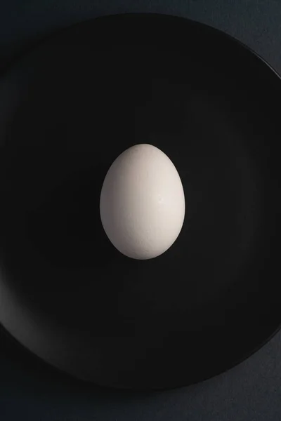 黒い皿の中の単一の白い卵暗いムーディプレーン最小限の背景 トップビュー 幸せなイースターの日 — ストック写真
