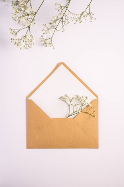 Beyaz boş kartlı Kraft kahverengi kağıt zarf, gypìila çiçekleri, beyaz arka plan, sahte boş mektup