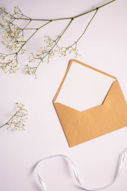 Beyaz boş kartla Kraft kahverengi kağıt zarf, gypìila çiçekleri ve kumaş kurdele, beyaz arka plan, boş harf