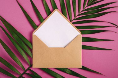 Palmiye yapraklarının üzerinde beyaz boş kart olan Kraft kahverengi kağıt zarf, pembe mor arkaplan, sahte boş mektup