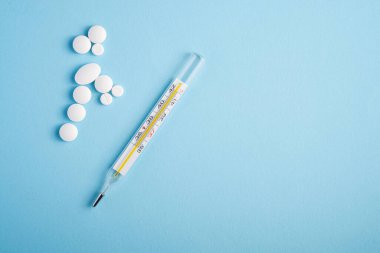 Parlak mavi arkaplan üzerine haplar, tabletler ve analog termometre, sağlık sigortası tıbbi konsepti, antibiyotikler ve tedavi, üst görünüm kopyalama alanı