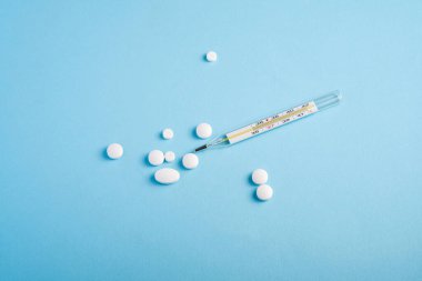 Parlak mavi arkaplan üzerine haplar, tabletler ve analog termometre, sağlık sigortası konsepti, antibiyotikler ve tedavi, açı görünümü kopyalama alanı