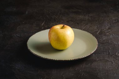 Gri plakalı taze, siyah desenli arka plan, açı manzaralı bir elma.