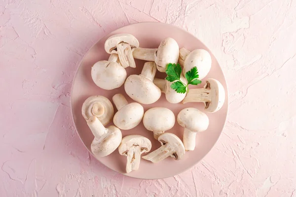 Champignon mushrooms healthy food on pink plate with parsley greenery on pink textured background, top view