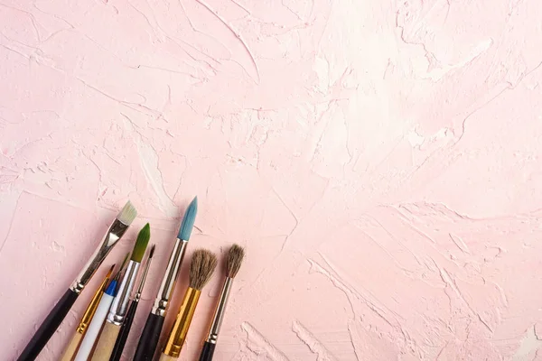 Paint brushes, artist tools for drawing on textured pink background, top view, copy space