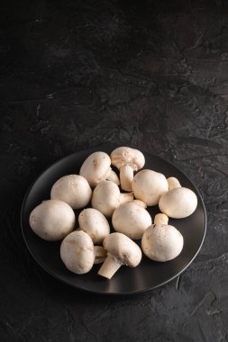 Champignon mantarları siyah tabaktaki sağlıklı yiyecekleri siyah desenli arka planda, açı görünümü kopyalama alanı