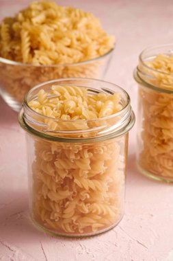 Cam kasede çiğ buğday sarmalı makarna ve dokulu pembe arka plan, açı manzaralı kavanoz.