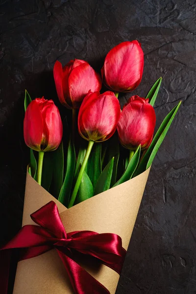 Bouquet with bow-knot ribbon of red tulip flowers on textured black background, top view copy space