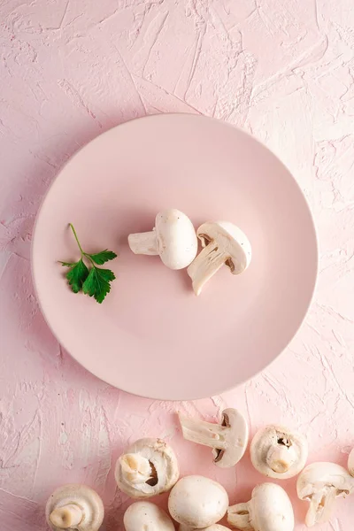 Champignon mushrooms healthy food on pink plate with parsley greenery on pink textured background, top view