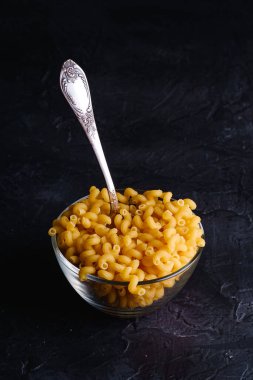 Cam kase ve kaşık, kavunlanmamış altın buğday, kıvırcık makarna, dokulu siyah arka plan, açı manzaralı.