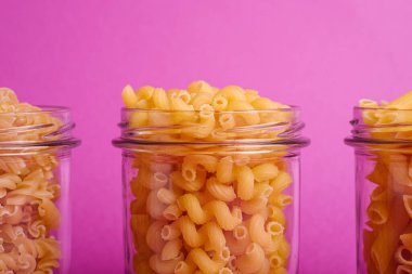 Asgari pembe arka planda, çeşitli pişirilmemiş altın buğday makarnalı üç cam kavanoz, açı açılı makro.