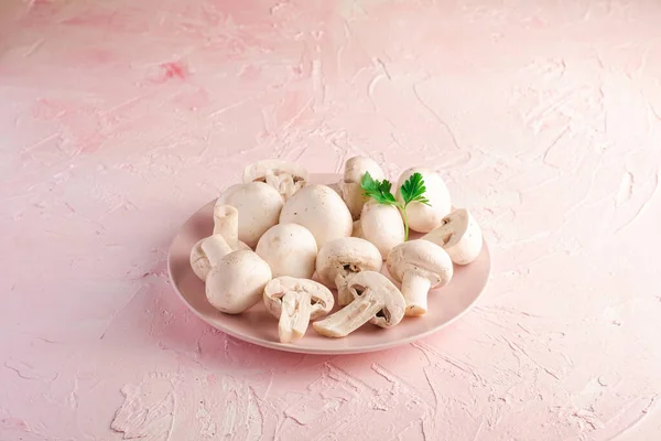 Champignon mushrooms healthy food on pink plate with parsley greenery on pink textured background, angle view