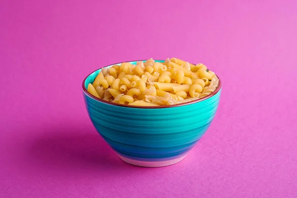 蓝色碗 各种未煮熟的金黄色面食 粉红底色最低 角度视图 — 图库照片