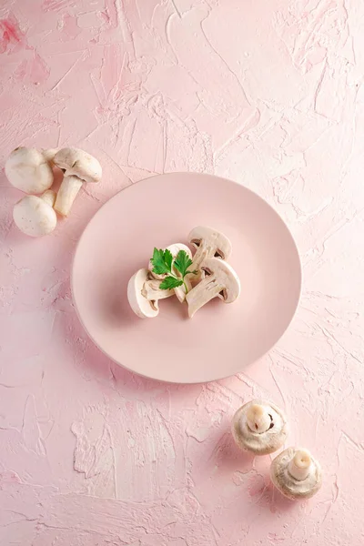 Champignon mushrooms healthy food on pink plate with parsley greenery on pink textured background, angle view copy space